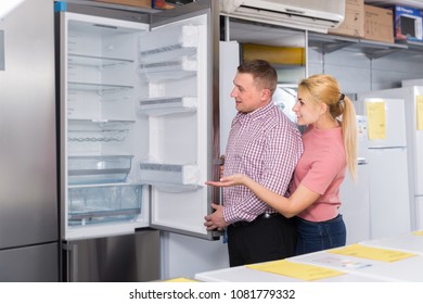 Positive family couple chooses refrigerator in store of household appliances  