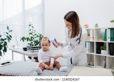 Positive Family Doctor Checking Temperature Of Baby Boy With Pyrometer In Clinic