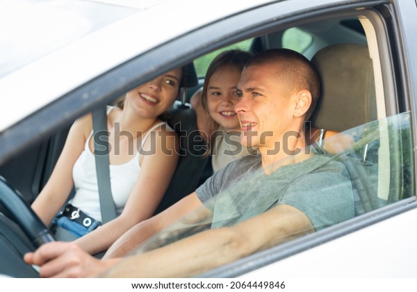 Positive family of three driving in the car\
with open windows, they talking and\
laughing