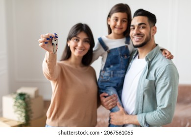 Positive family of three showing house key, standing in living room of new home, selective focus hand. Parents and daughter happy to move to bigger apartment, holding flat key, blurred background - Shutterstock ID 2067561065