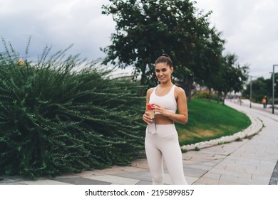 Positive Female Athlete In Activewear Smiling And Looking At Camera While Standing On Walkway In Green City Park On Cloudy Day