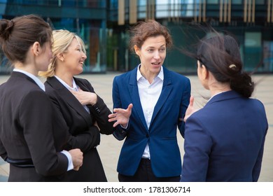 Positive Female Coworkers Talking Outdoors. Businesswomen Wearing Suits Standing Together In City. Work Discussion And Business Colleagues Concept