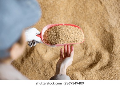 Positive female farm worker holding scoop with soybean hulls, natural cattle feed, at farm storage - Powered by Shutterstock