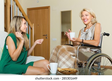 Positive female friend visiting disabled woman on chair indoor