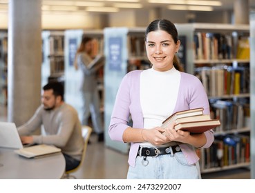 Positive female librarian standing near bookshelves with book in hands - Powered by Shutterstock