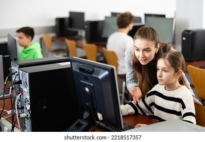 Positive Female Teacher Helping Concentrated Teen Schoolgirl Studying In College Library Computer Lab..