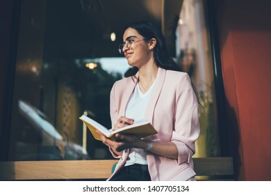 Positive Female Writer Sitting Outdoors And Creating New Charter Of Best Seller Thoughtful Looking Away And Thinking On Positive Idea For Making Notes In Knowledge Textbook, Notepad For Education