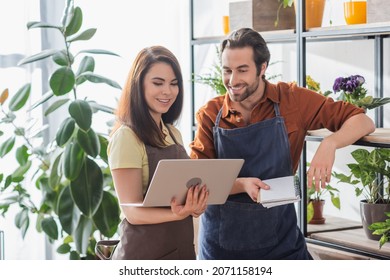 Positive florists with laptop and notebook working near plants in shop - Shutterstock ID 2071158194