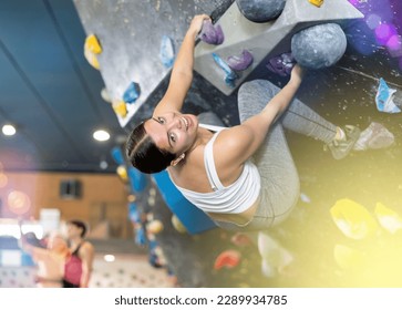 Positive focused young woman exercising on black climbing wall without safety belts and preparing for summer mountain hiking in game center indoors - Powered by Shutterstock