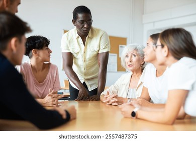 Positive friendly African American English tutor giving language courses to group of interested adults of different ages and nationalities sitting around table in classroom.. - Powered by Shutterstock