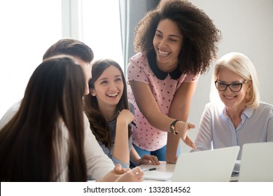 Positive friendly african and caucasian creative team employees talking laughing at company meeting, happy cheerful diverse workers group having fun involved in corporate office funny teambuilding