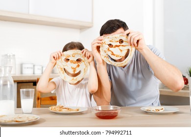 Positive friendly daughter and father make funny faces from pancakes, looks through handmade eyes, sit at kitchen, have breakfast, wait for mother. People, relationship, culinary, family concpet.