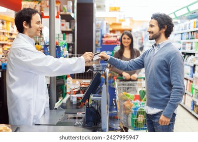 A positive and friendly interaction at the grocery store checkout counter between a smiling male cashier and a cheerful female customer in casual clothing - Powered by Shutterstock