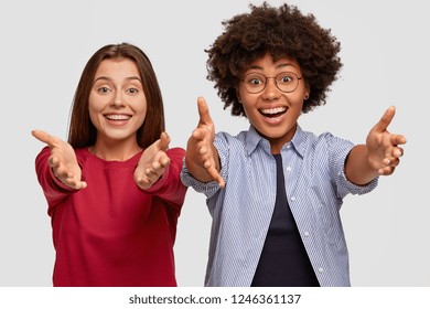 Positive friendly looking multiethnic women stretch hands at camera, going to embrace someone with warm hug, smile broadly, express good attitude, isolated over white background. Come here, my dear - Powered by Shutterstock