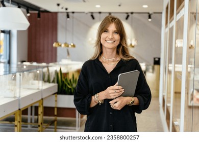 Positive friendly mature middle age beautiful female business owner in a jewelry shop, portrait. - Powered by Shutterstock