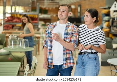 Positive friendly young adult couple, guy and girl, looking with interest for comfortable furniture for patio and garden of country house in home decor store - Powered by Shutterstock