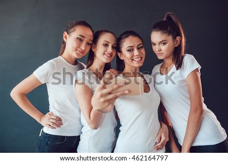 Positive friends portrait of happy girls making selfie, sure funny faces, grimaces, joy, emotions, casual style, pastel colors. Dark background.