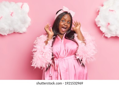 Positive Funny Dark Skinned Chubby Adult Woman With Long Hair Keeps Mouth Opened Has Long Nails Long Hair Wears Dressing Gown Feels Glad Spends Free Time At Home Isolated Over Pink Background