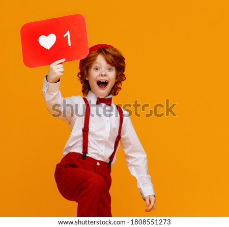 Positive ginger boy in stylish outfit demonstrating board with like symbol and looking at camera with opened mouth while promoting social media against yellow background
