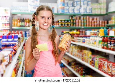 Positive Glad  Cheerful Smiling Tween Girl Choosing Food Products On Shopping List In Supermarket