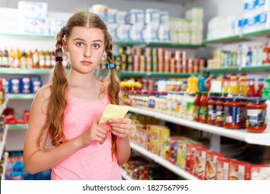 Positive Glad Cheerful Tween Girl Choosing Food Products On Shopping List In Supermarket