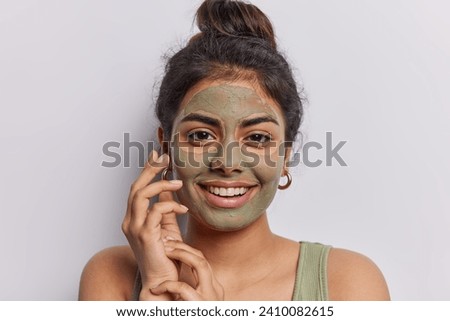 Positive good looking young Iranian woman touches face gently smiles gladfully looks directly at camera with happy expression isolated over white background. Beuaty procedures and wellness concept