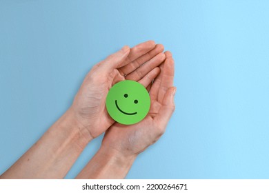 A Positive Green Smiley Face Inside Female Hands Against A Lovely Blue Paper Background.