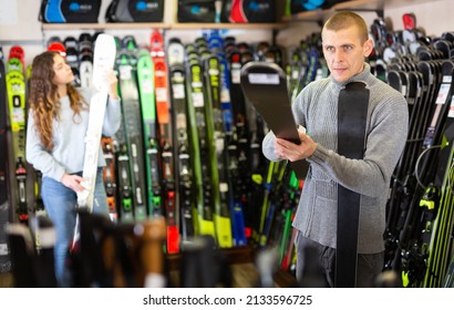 Positive Guy And Girl Are Choosing Skis In A Sports Equipment Store