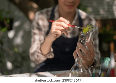 A positive and handsome young Asian man is handcrafting a decorative bottle, coloring a glass bottle with acrylic color in his home garden. Leisure and creative activity concepts - Powered by Shutterstock