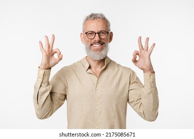 Positive happy caucasian mature middle-aged man smiling with toothy smile wearing glasses showing okay gesture with both hands isolated in white background