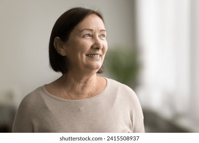 Positive happy elderly woman in casual cloth looking at window away, smiling, dreaming, planning good retirement, thinking on medical insurance, healthcare. Senior female model indoor casual portrait - Powered by Shutterstock