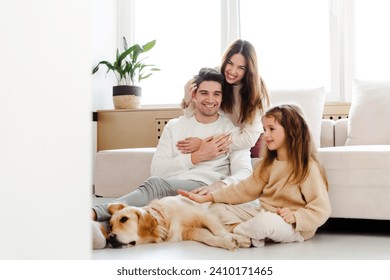 Positive happy family, beautiful woman hugging husband, little girl playing with dog, golden retriever, sitting in room in cozy home. Concept of harmony, parenthood, care - Powered by Shutterstock