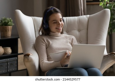 Positive Happy Gen Z Student Girl Wearing Headphones, Talking To Teacher, Tutor In Video Call, Watching Learning Webinar, Class, Lesson On Laptop, Attending College Conference, Writing Notes