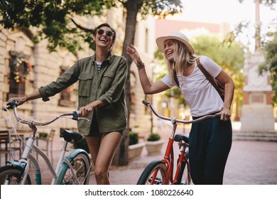 Positive and happy girls walking on the city street with bicycles. Female friends enjoying a walking down the street with their bikes. - Powered by Shutterstock