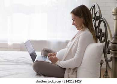 Positive Happy Late Pregnant Woman Using Laptop Computer, Sitting In Lotus Pose On Comfortable Bed, Talking On Video Call, Laughing. Expecting Mom Consulting Doctor Online, Watching Movie