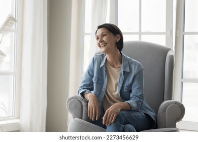 Positive happy pretty mature lady resting in comfortable armchair at home, looking at away, smiling, laughing, thinking. Senior woman enjoying leisure in cozy apartment - Powered by Shutterstock