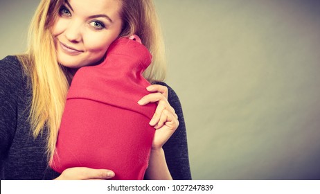 Positive Happy Woman Hugging Warm Hot Water Bottle In Red Soft Fleece Cover, On Grey. Health Care, Pain Relievers, Treatment Objects Concept.