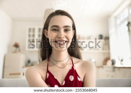 Positive happy young 20s girl in red sleeveless top home head shot portrait. Video call screen view of pretty young woman, natural beauty care model with thick eyebrows, imperfect toothy smile