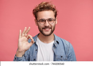 Positive Hipster Guy Shows Ok Sign, Demonstares That Everything Is Fine, Agrees With People Who Surrounds Him. Confident Cheerful Man Gestures Indoors. Body Language And Human Emotions Concept