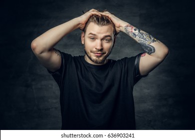 A Positive Hipster Male Dressed In A Black T Shirt Holds Head With Tattooed Arms.