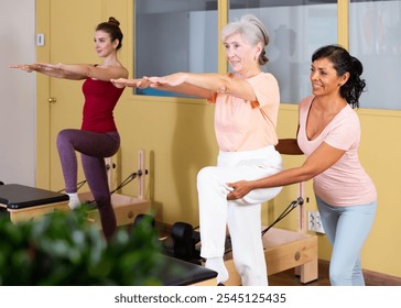 Positive Hispanic woman professional pilates instructor helping aged woman doing exercises on wunda chair. Wellness concept for elderly - Powered by Shutterstock