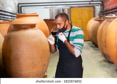 Positive House Sommelier In Protective Mask Tasting Red Wine From Barrels