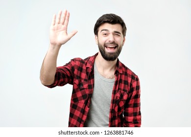 Positive Human Emotions. Friendly Looking Polite Young Hispanic Man Dressed In Checkered Shirt Saying Hi, Waving With His Hand