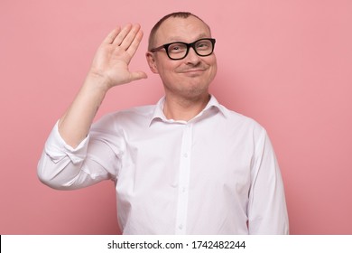 Positive Human Emotions. Friendly Looking Polite Mature Man Saying Hi, Waving With His Hand. Studio Shot On Pink Wall