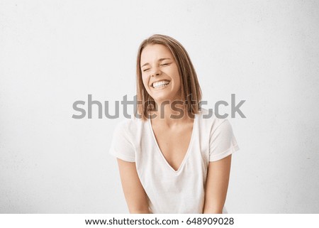 Positive human emotions. Headshot of happy emotional teenage girl with bob haircut laughing from the bottom of her heart, keeping eyes closed, showing perfect white teeth while having fun indoors