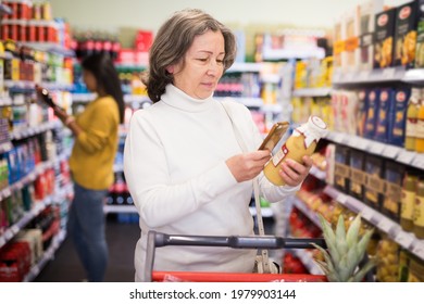 Positive Interested Elderly Woman Scanning Barcode On Bottle Of Fruit Juice With Her Smartphone, Checking Product Information. Concept Of Modern Technologies For Convenience Of Buyers