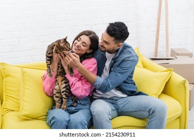 Positive Interracial Couple Petting Bengal Cat On Couch At Home