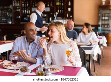 Positive Interracial Married Couple Sitting In Cozy Restaurant And Eating Pizza With Wine