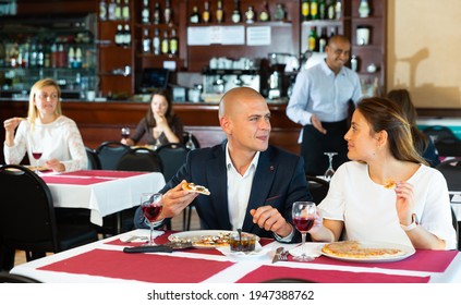 Positive Interracial Married Couple Sitting In Cozy Restaurant And Eating Pizza With Wine