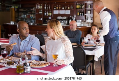 Positive Interracial Married Couple Sitting In Cozy Restaurant And Eating Pizza With Wine